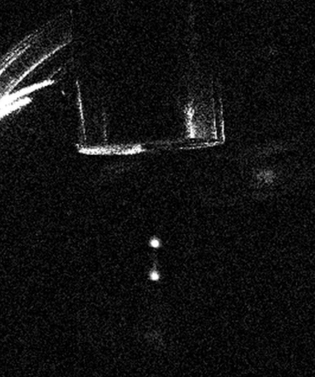 Auf diesem Foto sieht man, wie Cluster aus etwa 10.000 Cäsiumatomen in der Vakuumkammer schweben. Sie werden von gekreuzten Laserstrahlen in der Schwebe gehalten, die ein stabiles optisches Gitter erzeugen. Oben sind ein zylindrisches Wolframgewicht und seine Halterung zu sehen.