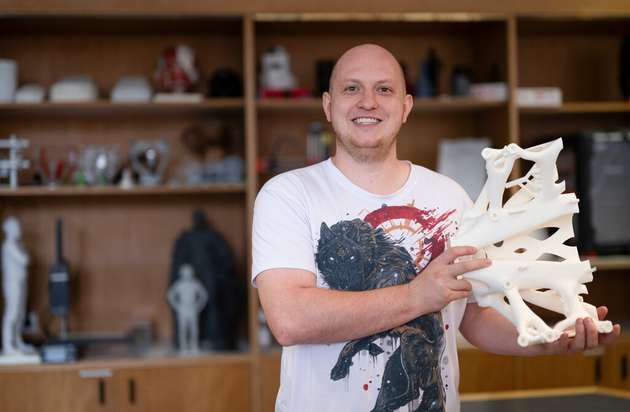 Felix Felgenträger zeigt einen 3D-gedruckten Vakuumgreifer. Im Regal im Hintergrund stehen weitere Exponate aus dem 3D-Druck-Spektrum der Hochschule Coburg wie die bekannte 3D-gedruckte Coburger Prinz-Albert-Statue.